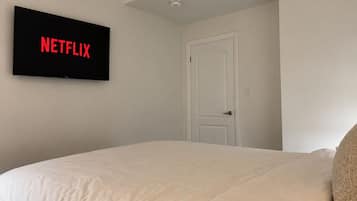 A bedroom with a bed, a door, and a wall-mounted television displaying 'NETFLIX'.
