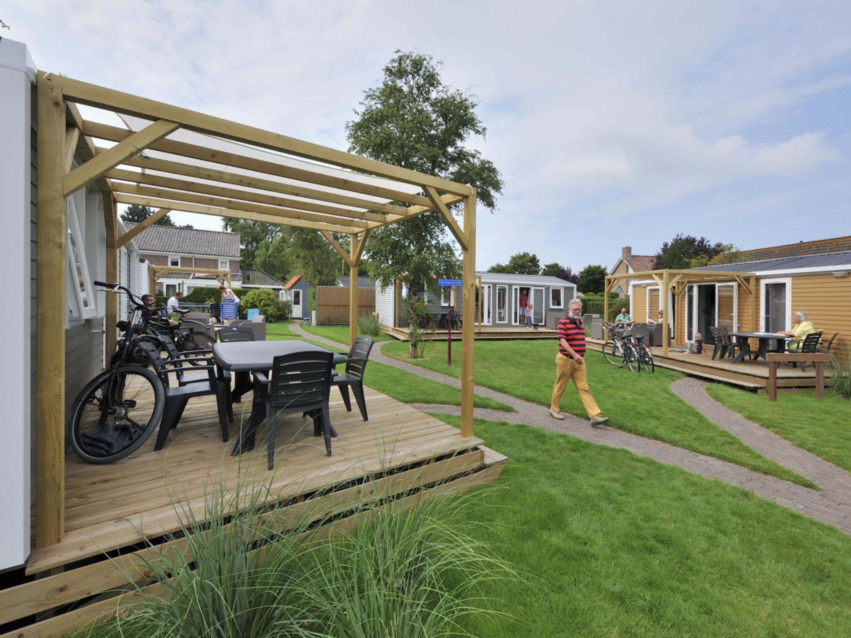 A wooden deck with a table and chairs, a covered patio area, and a grassy yard with a walking path.
