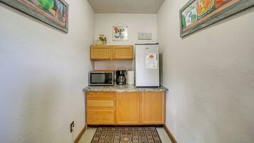 A compact kitchen with wooden cabinets, a microwave, a coffee maker, and a refrigerator.