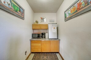 Eine kompakte Küche mit Holzausstattung, einer Mikrowelle, einer Kaffeemaschine und einem Kühlschrank.