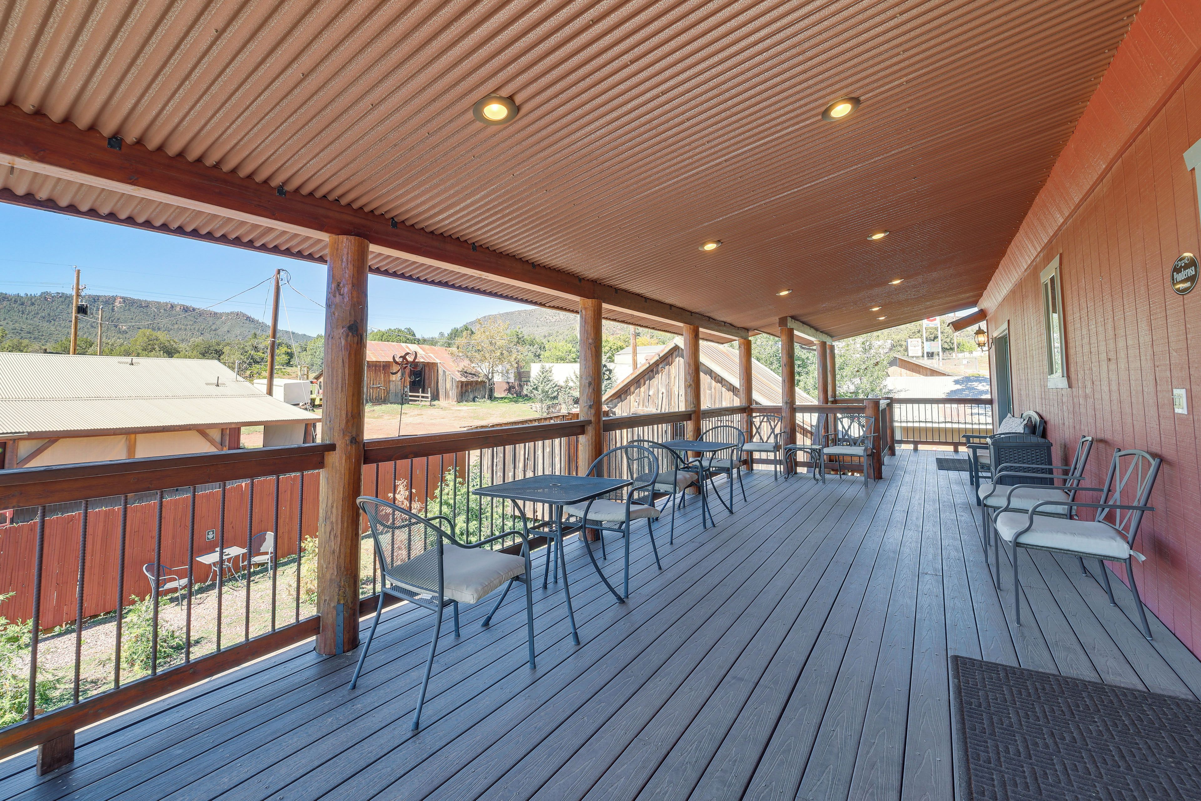 Eine überdachte Terrasse im Freien mit Holzboden, Metalltischen und -stühlen und Blick auf die umliegende Landschaft.