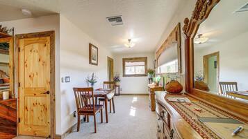 A hallway with a wooden door, a dining area with chairs and a table, a mirror, and a window with natural light.