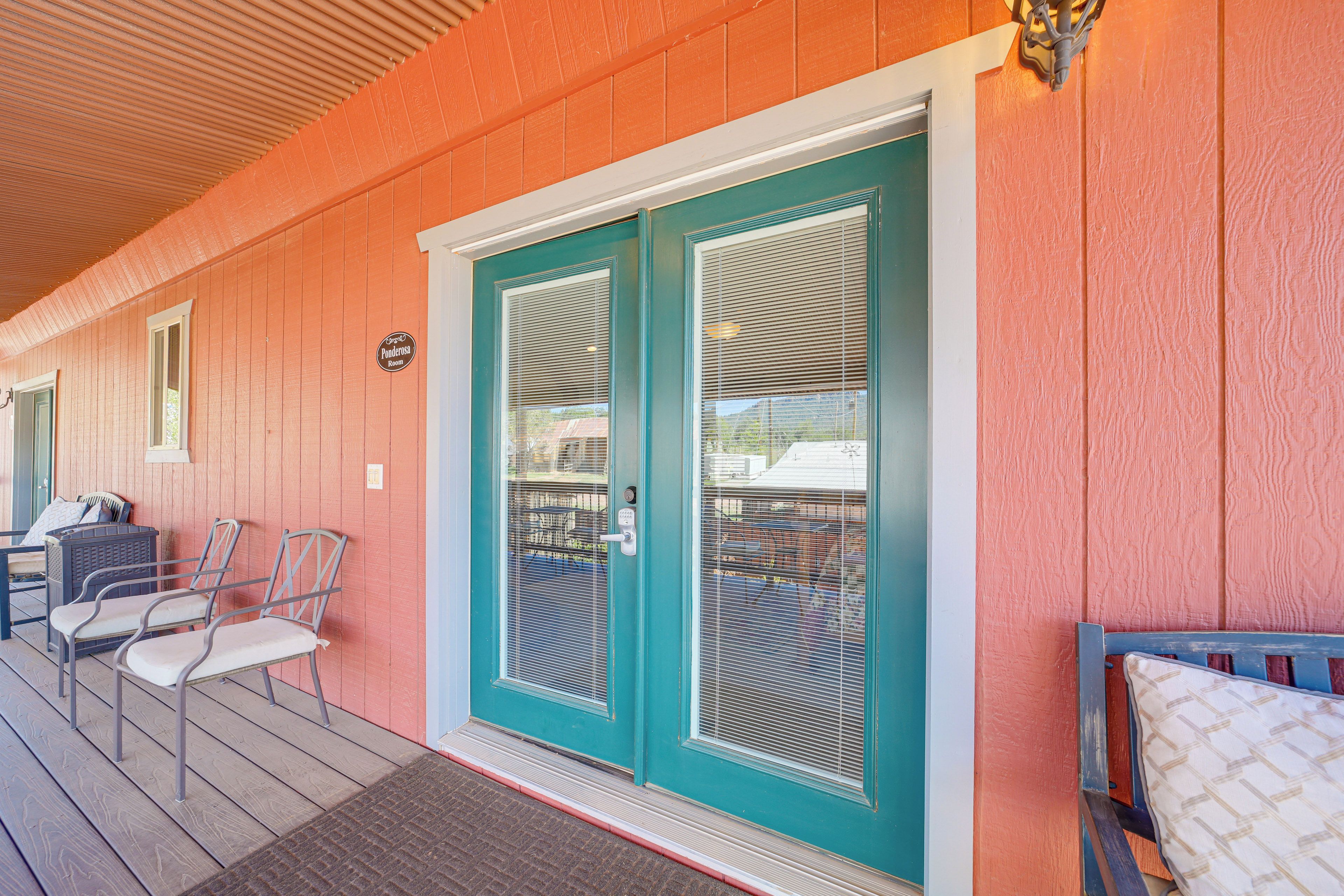 A covered porch with a teal door, a small seating area with chairs, and a sign indicating a room named 'Ponderosa Room'.