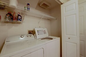 A laundry area with a Whirlpool washer and dryer, a shelf with cleaning products, and a white door. - Spacious Hillsboro Home w/ Fenced Yard (Hillsboro)