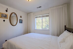 Ein Schlafzimmer mit einem Einzelbett, einem Fenster mit Vorhängen, einem Wandspiegel und zwei gerahmten Bildern.