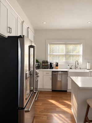 A modern kitchen with stainless steel appliances, white cabinetry, and a large window with blinds. - Spacious 3BR East Side Home, Near Brown & Miriam (Providence)