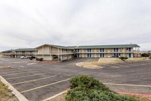 A motel with a central parking lot, multiple motel units, and a small landscaped area. - 1 FULL BED | MOBILITY ACCESS RI SHWR, NSMK (Albuquerque)