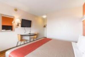 Ein Hotelzimmer mit einem Bett, einem Schreibtisch, einem Sessel, einem an der Wand befestigten Fernseher und einem Fenster.