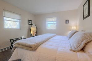A bedroom with a bed, two windows, a mirror, and a lamp.