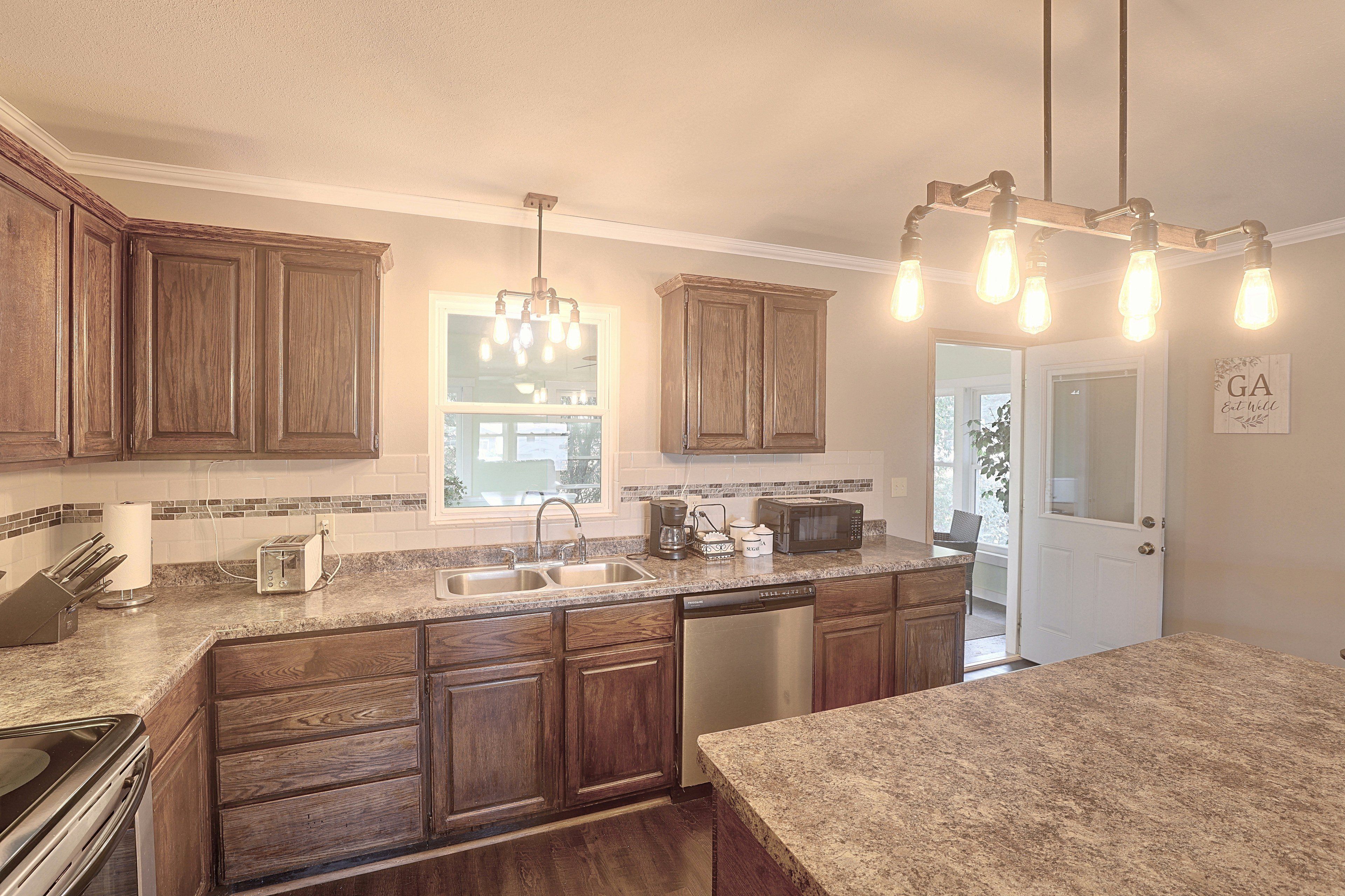 A kitchen with wooden cabinets, a granite countertop, a built-in dishwasher, and a window above the sink.