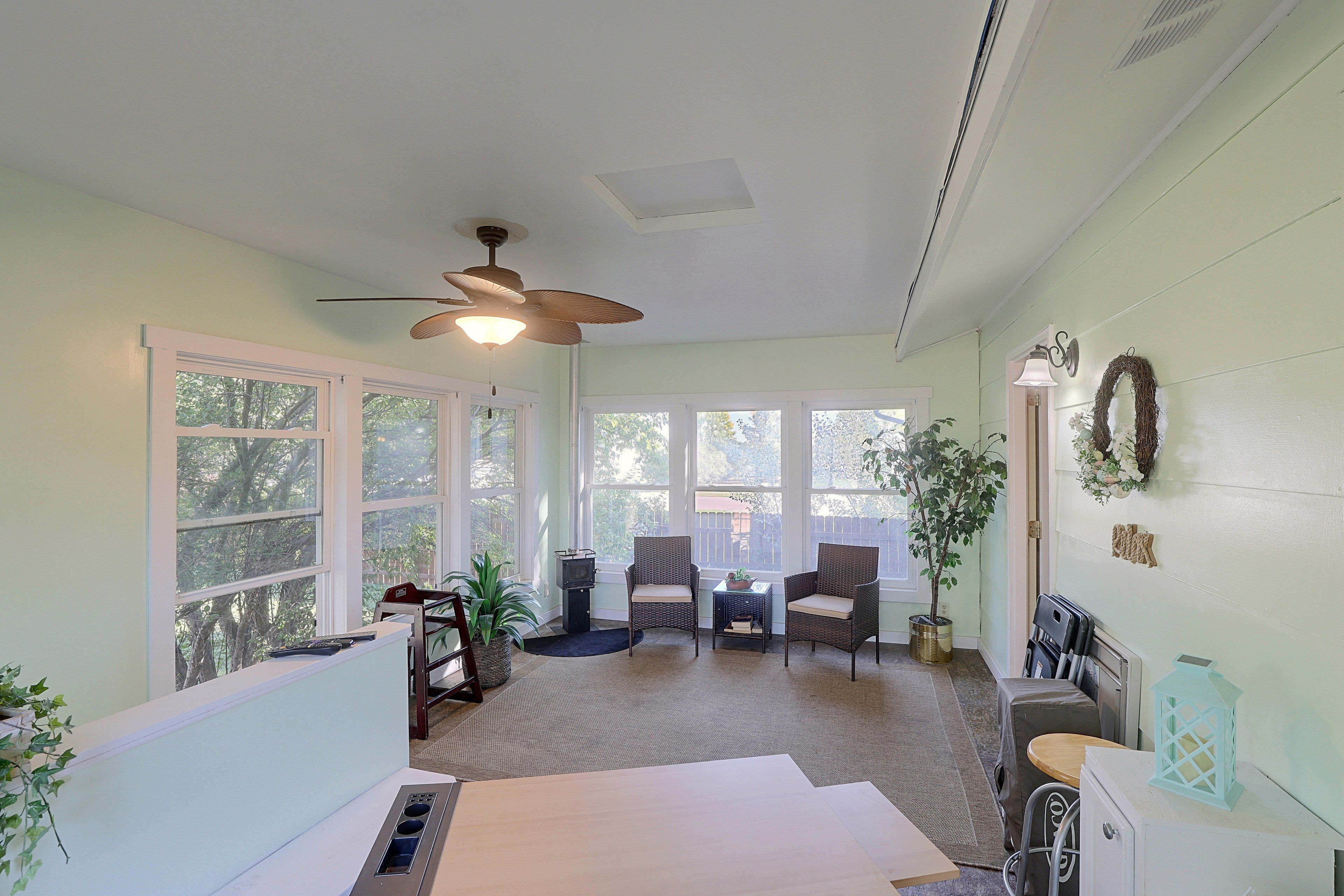 A sunroom with large windows, a ceiling fan, wicker furniture, and a small table with a plant.