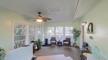 A sunroom with large windows, a ceiling fan, wicker furniture, and a small table with a plant.