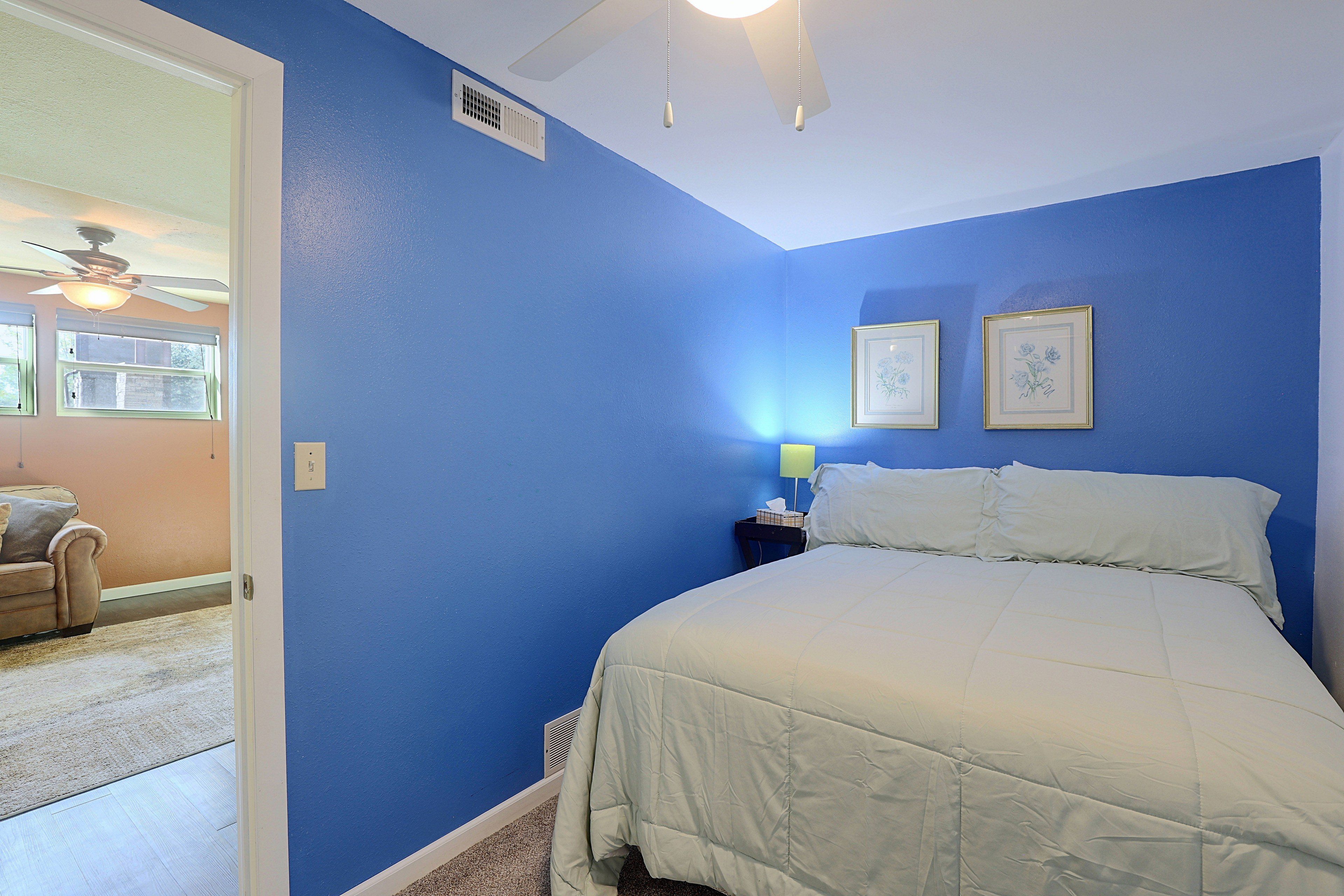 A bedroom with a bed, a nightstand, a ceiling fan, and two framed pictures on the wall.