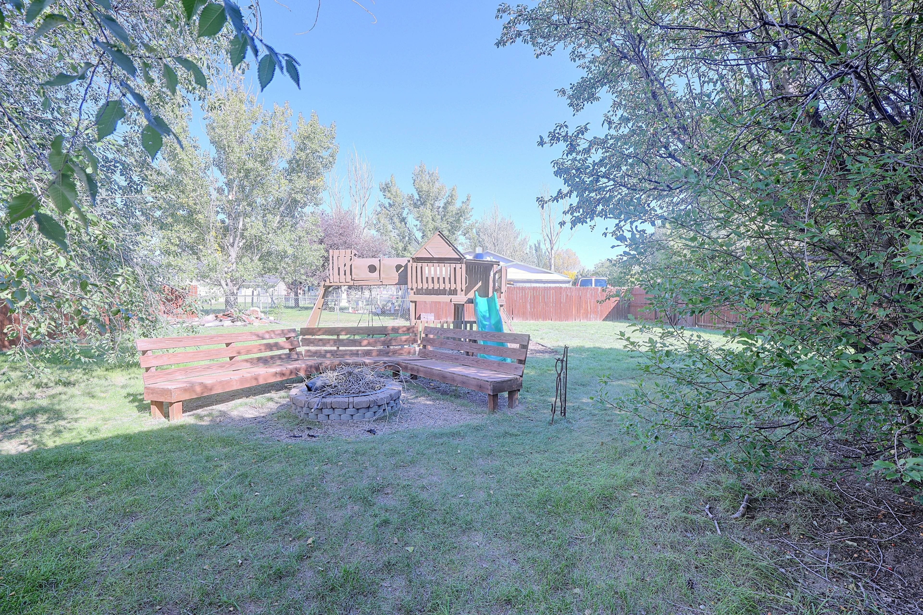 A wooden play structure with benches and a fire pit in a grassy yard.