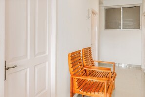 A hallway with white walls, a wooden bench, and a door with a window.