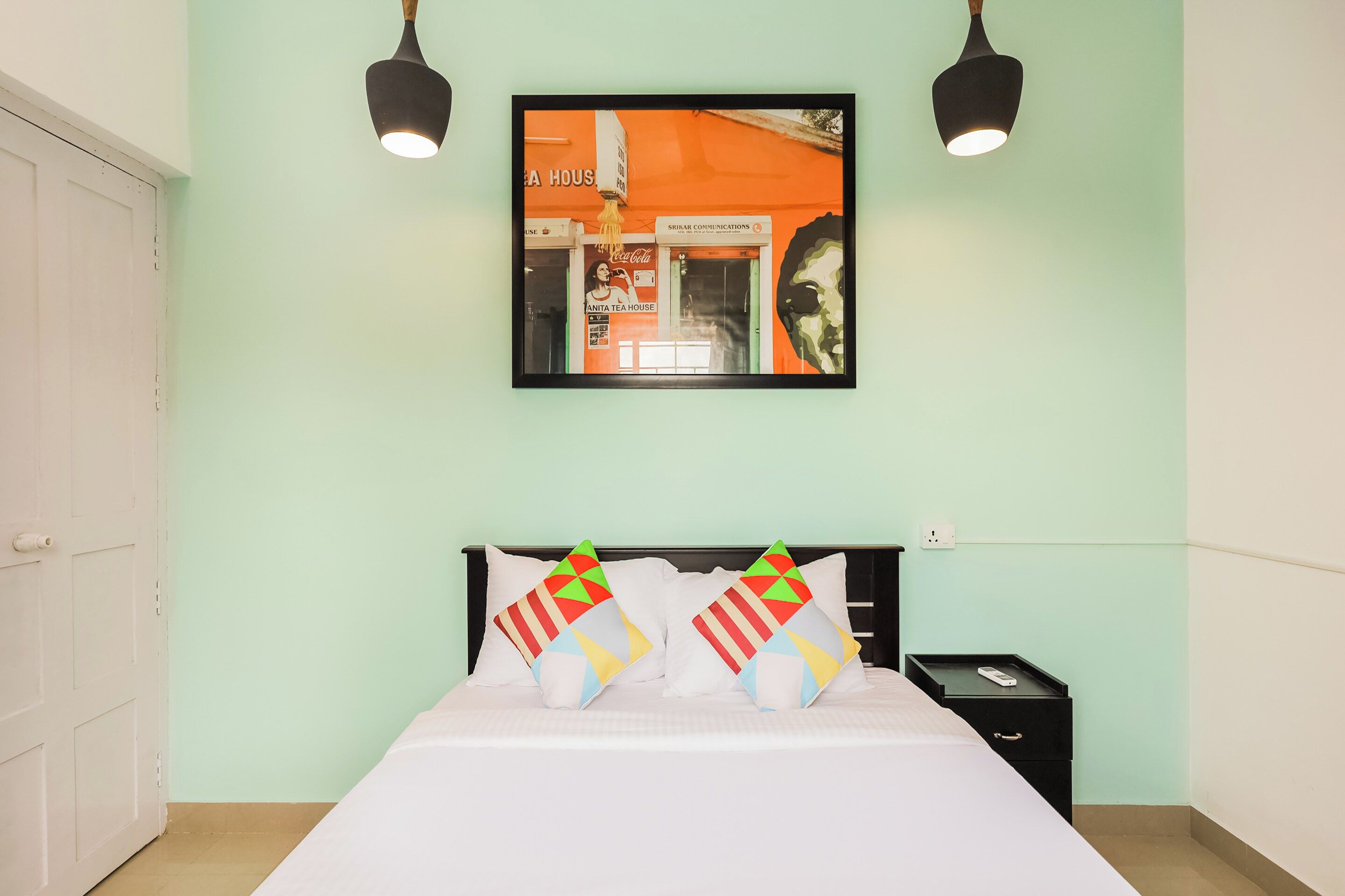 Un dormitorio con cama, almohadas, una mesita de noche, un cuadro en la pared y dos lámparas de pared.