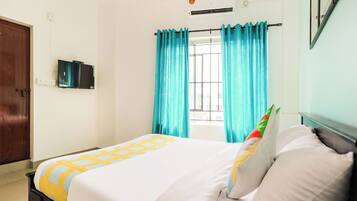 Habitación de hotel con cama, ventana con cortinas, aire acondicionado y televisor montado en la pared.