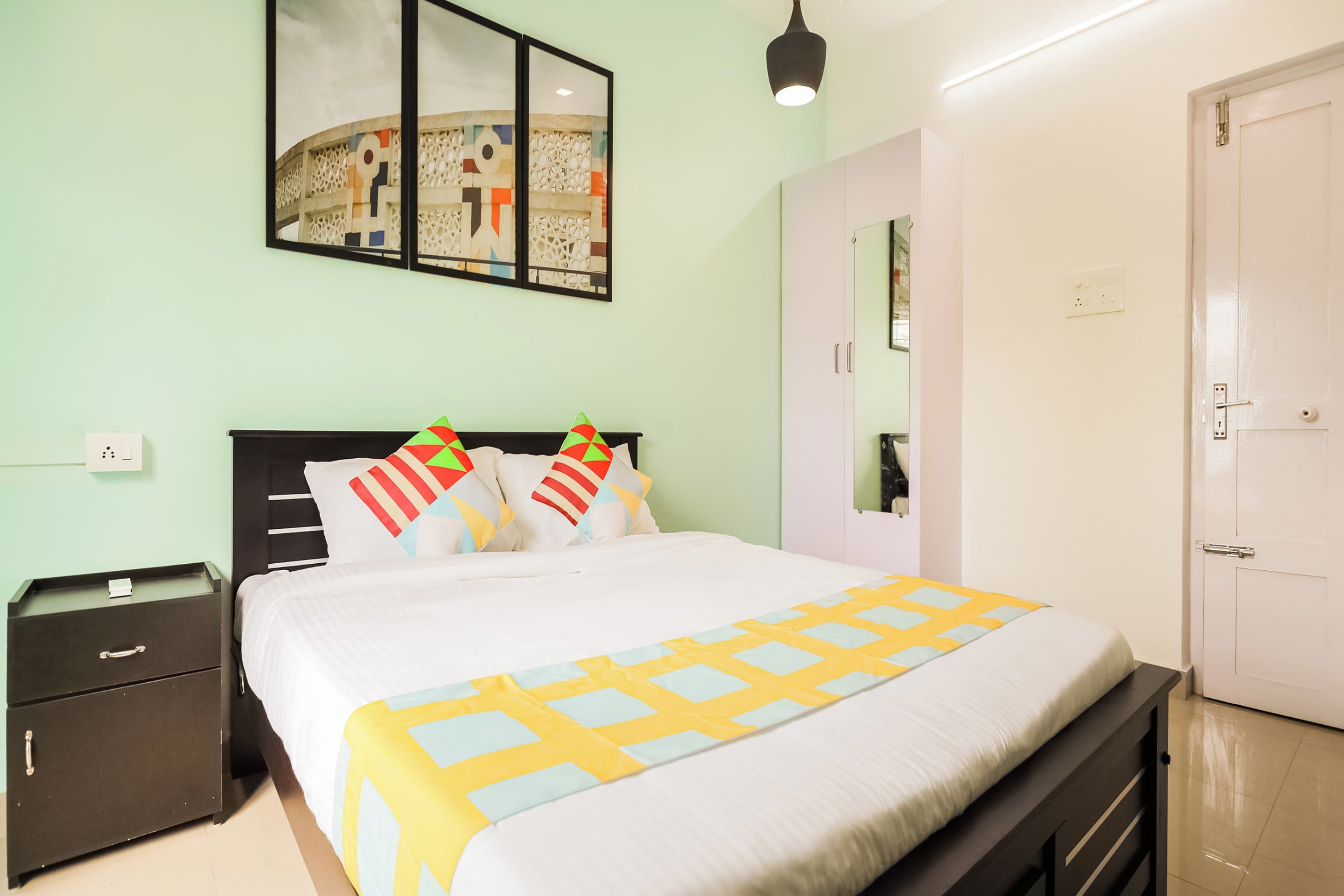 Un dormitorio con cama, mesita de noche, armario, espejo y puerta.