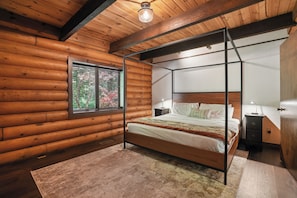 Ein Schlafzimmer in einer Blockhütte mit einem Himmelbett, einem Fenster mit Jalousien, einem Nachttisch und einem Beistelltisch.