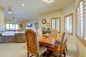 A dining area with a wooden table and patterned chairs, a kitchen in the background, and a clock on the wall. - Desert Hills Fenced Acre! Pool, Spa + Dogs Allowed (New River)