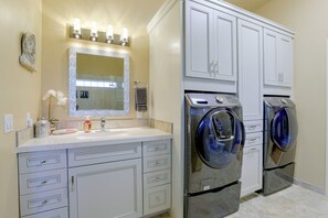 A modern bathroom with a vanity, a mirror, a sink, and two front-loading washing machines. - Desert Hills Fenced Acre! Pool, Spa + Dogs Allowed (New River)