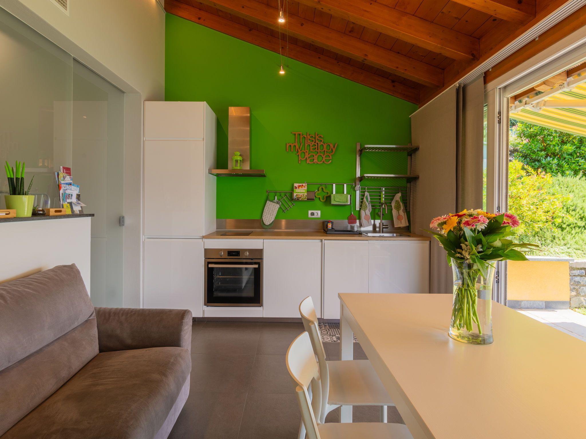 Una cucina moderna con una parete verde a contrasto, un forno a incasso e un'area pranzo con tavolo e sedie.