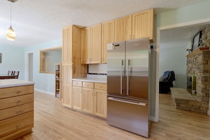 A kitchen with wooden cabinets, a stainless steel refrigerator, and a stone fireplace. - The Johnson Way: Cosby Home Near Gatlinburg (Cosby)