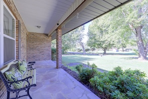 A covered porch with a brick wall, a bench, and a view of a grassy yard with trees. - The Johnson Way: Cosby Home Near Gatlinburg (Cosby)
