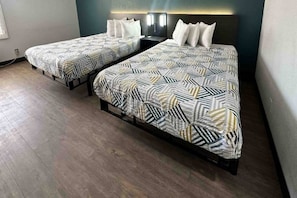 Two twin beds with patterned bedding, a nightstand with a lamp, and a wooden floor. - 2 Queen Beds | Non-Smoking (LEBEC)