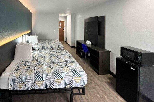 A hotel room with two beds, a desk, a TV, and a refrigerator. - 2 Queen Beds | Non-Smoking (LEBEC)