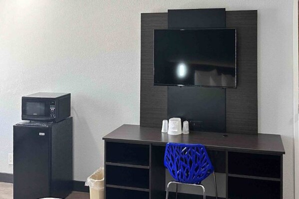 A compact room with a flat-screen TV mounted on a dark wall, a small black microwave on a cabinet, and a blue chair with a unique design. - 2 Queen Beds | Non-Smoking (LEBEC)