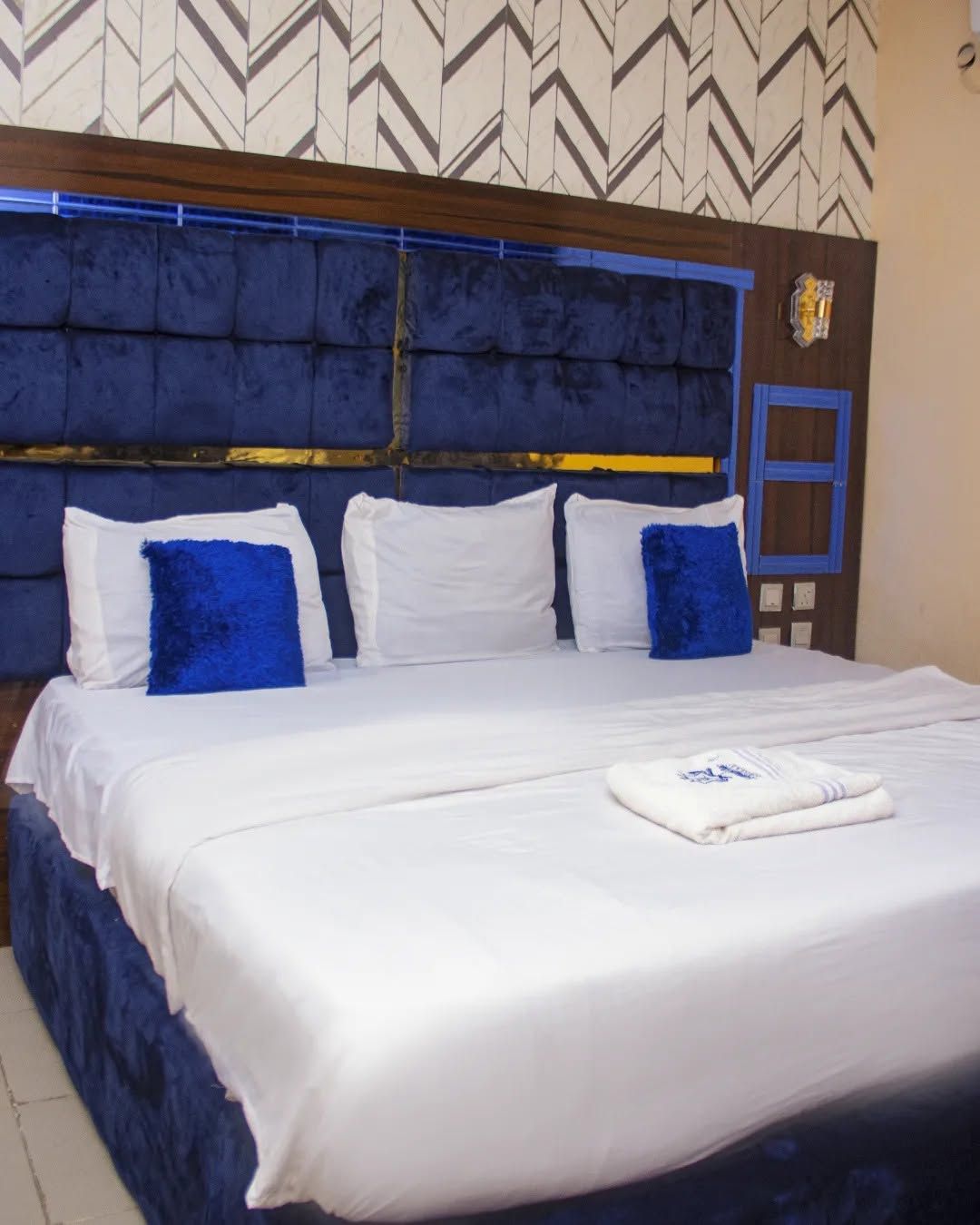 A hotel room with a large bed, a blue headboard, and a patterned wall.