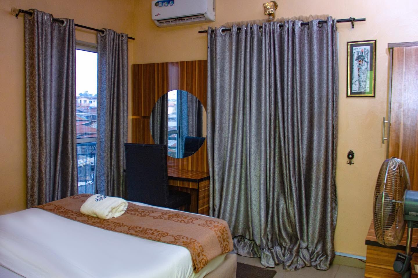 A hotel room with a bed, a mirror, a fan, and curtains.