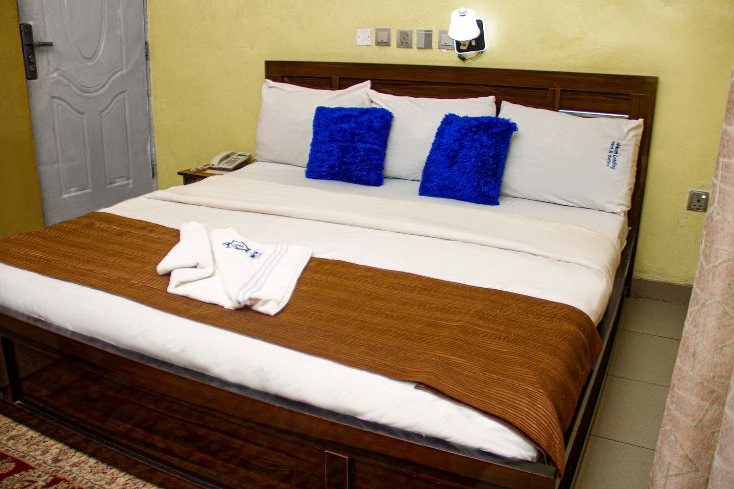 A neatly made bed with a brown blanket, two blue pillows, and a white towel on the bed.