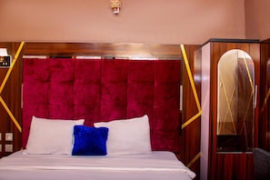 Une chambre d’hôtel avec un grand lit, une tête de lit rouge en tissu et un miroir au motif géométrique.