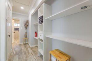 Un couloir avec un plancher en bois, des murs blancs et une porte blanche. On y trouve une petite table en bois et un vase contenant des plantes séchées.
