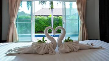 A bed with two towels arranged in the shape of swans, a window with curtains, and a view of greenery outside.