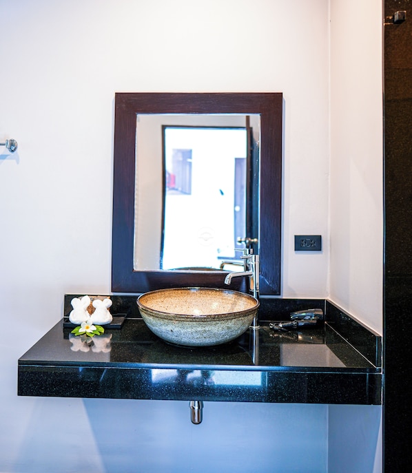 Une salle de bain avec un comptoir noir, un lavabo en céramique, un robinet et un miroir au-dessus du lavabo.