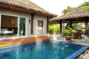 Un'area piscina con un pontile in legno, una sala con pareti in vetro e una struttura con tetto di paglia.