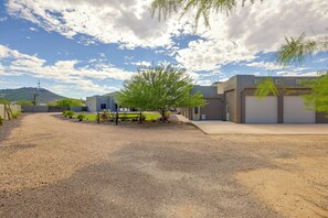 A residential area with a gravel driveway, a small tree, and a modern building with a garage. - Mtn-View Couple’s Stay in Desert Hills Near Trails (New River)