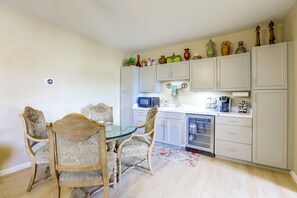 A compact kitchen with white cabinets, a microwave, a coffee maker, and a refrigerator. There is a dining table with chairs and a small rug on the floor. - Mtn-View Couple’s Stay in Desert Hills Near Trails (New River)