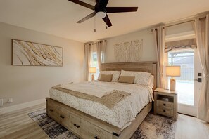A bedroom with a bed, nightstands, a ceiling fan, a wall-mounted macrame piece, and a window with curtains. - Florida Sunshine! Cape Coral Home w/ Pool (Cape Coral)