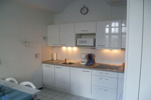 A compact kitchen with white cabinets, a microwave, a sink, and a clock on the wall. - Seagull's Nest III Apartment 11 (Borkum)