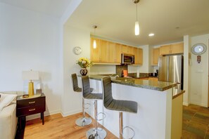A modern kitchen with a central island, bar stools, stainless steel appliances, and wooden cabinets. - Walk to Gaslamp & Petco Park! Dtwn Apt w/ Balcony (San Diego)