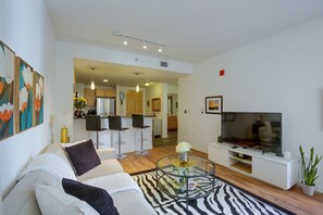 A modern living room with a sofa, a coffee table, and a TV. There is a kitchen area in the background. - Walk to Gaslamp & Petco Park! Dtwn Apt w/ Balcony (San Diego)
