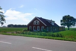 A single-story house with a gabled roof and a small porch, surrounded by a green field and a clear sky. - Holiday home in Bunde with swimming pool (Bunde)