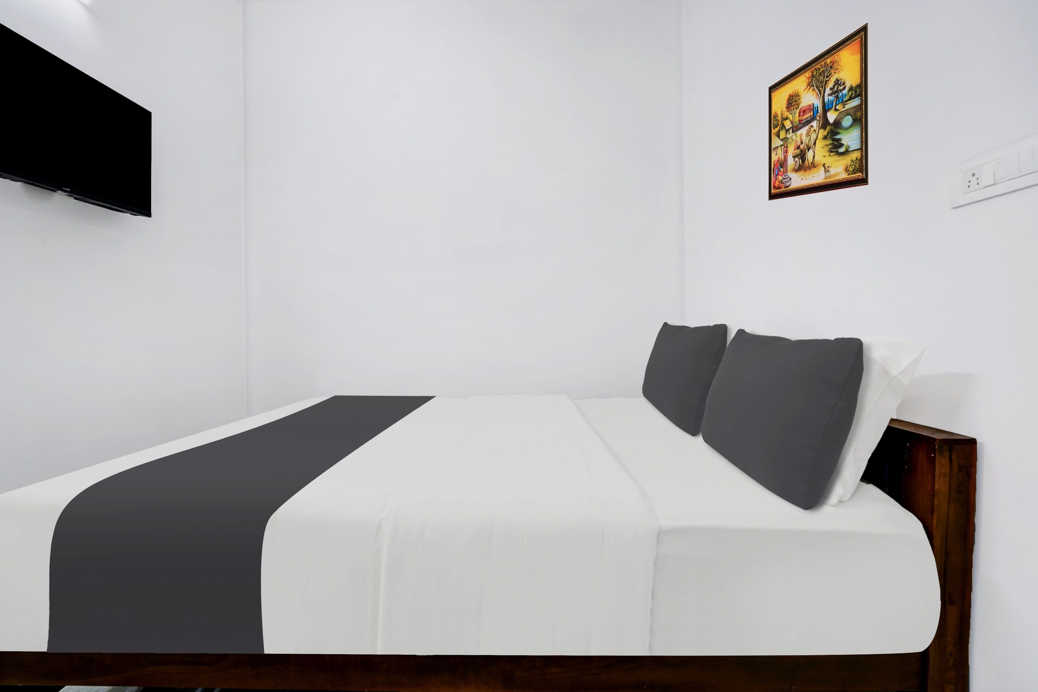 A hotel room with a bed, a flat-screen TV mounted on the wall, and a painting above the bed.