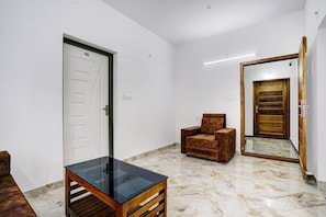 A room with a white door, a brown armchair, a glass-top table, and a wooden-framed mirror on the wall. - Hotel O EVA RESIDENCY (Kochi)