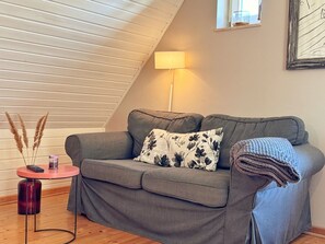 A cozy room with a grey sofa, a small round table with a lamp, and a window with a view. - defaultName (Glowe)