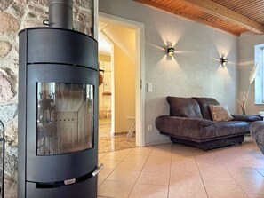 A modern living room with a stone wall, a black wood-burning stove, a leather sofa, and two wall-mounted lights. - defaultName (Glowe)